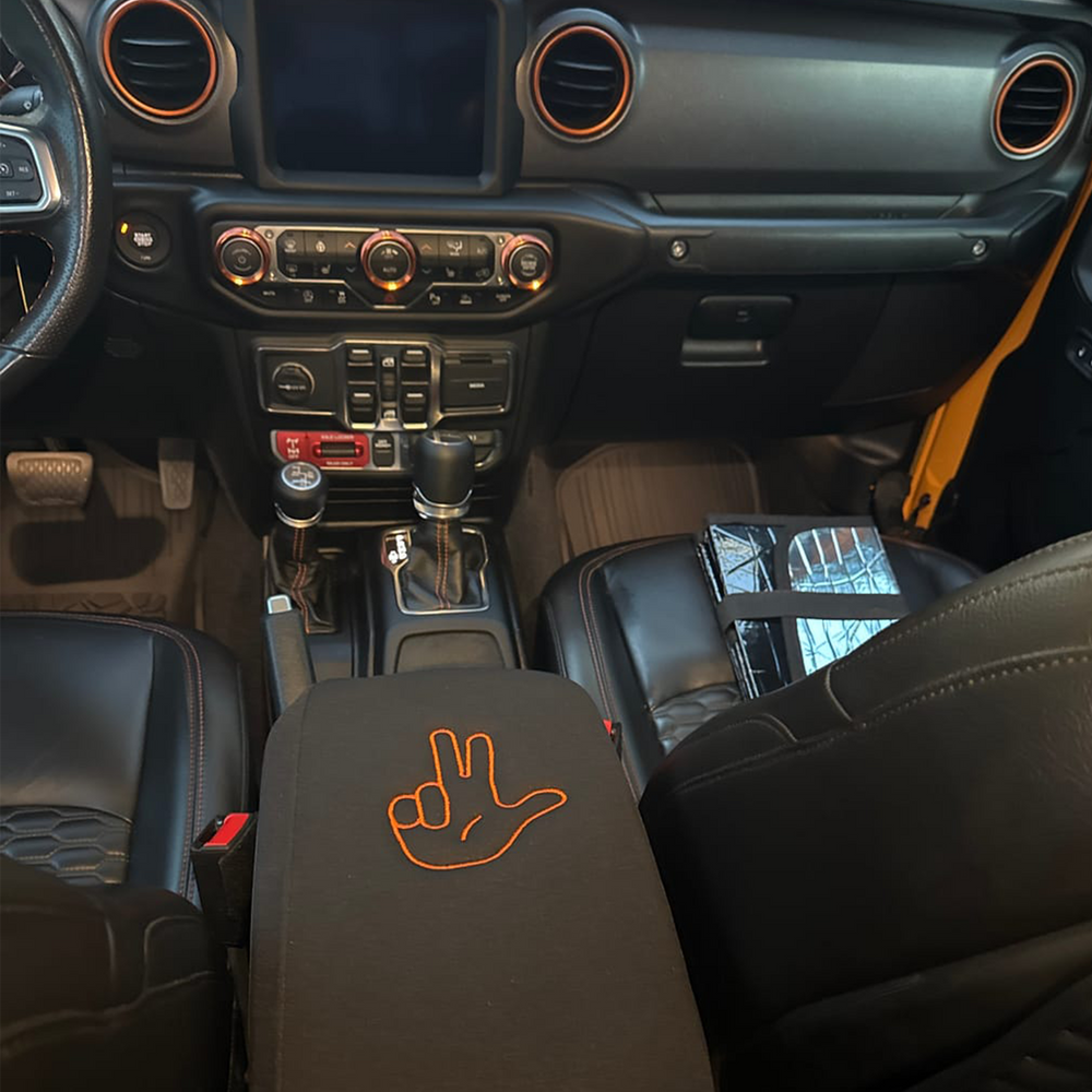Car interior with a "Jeep Life" hand gesture design on the console armrest cover in orange.